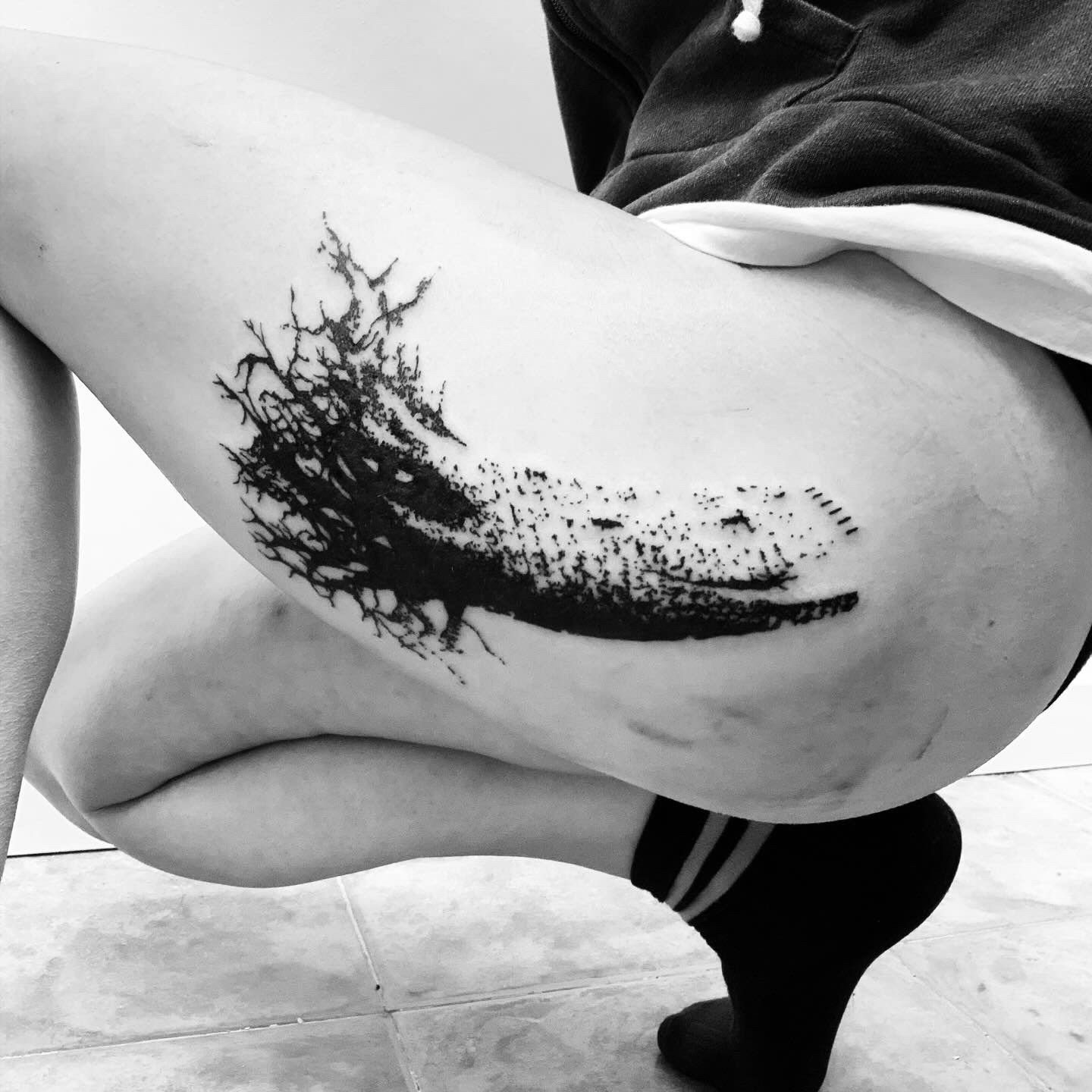 Una mujer tiene un tatuaje en blanco y negro en el muslo.