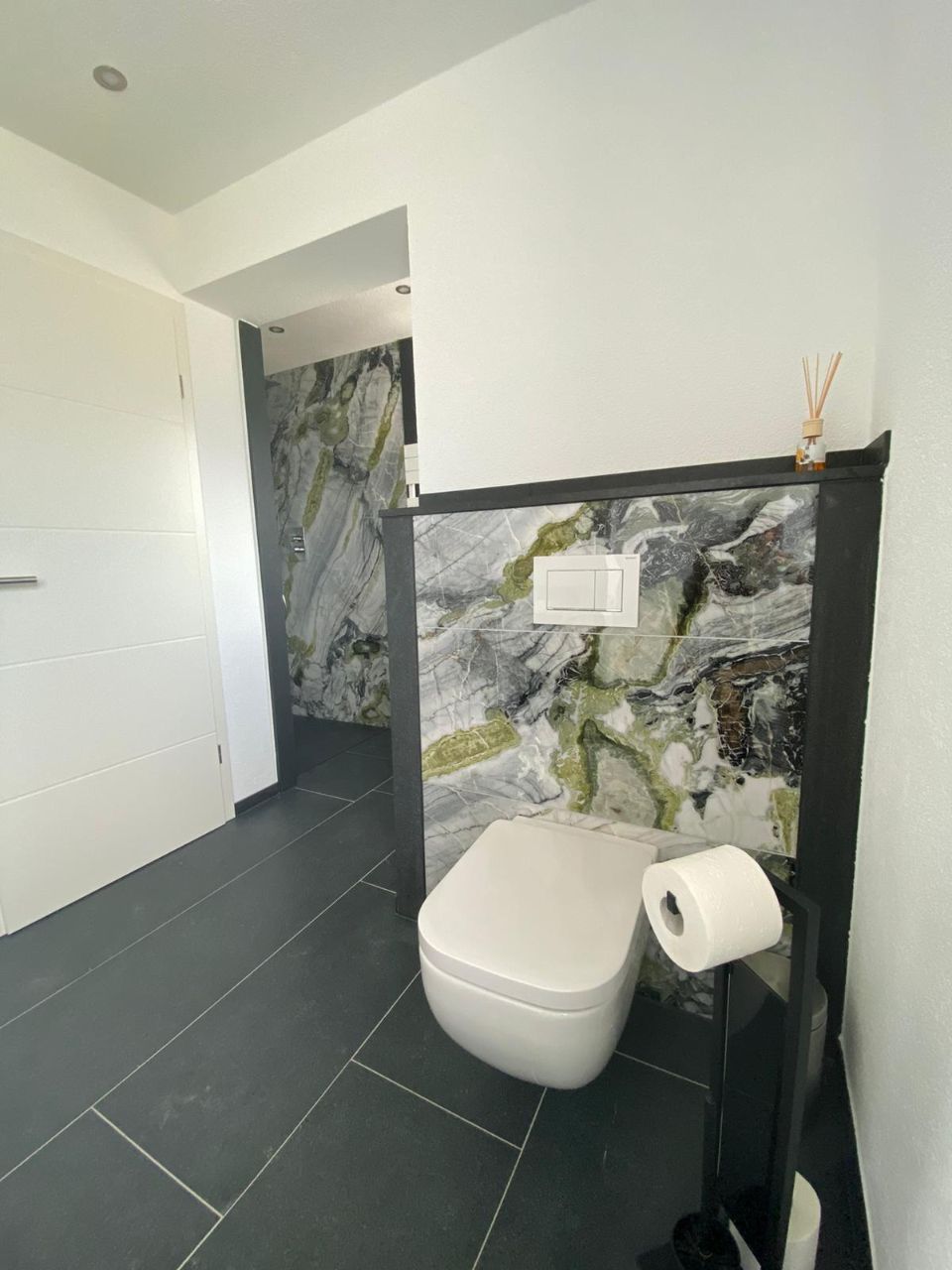 Toilette mit Natursteinelementen an der Wand und schwarzem Fliesenboden