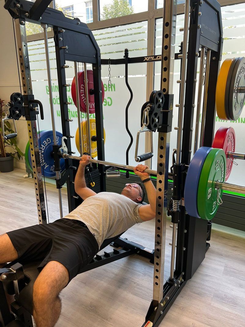 Ein Mann macht Bankdrücken im Fitnessstudio. Er liegt auf einer Bank und stemmt eine Langhantel an einer Smith-Maschine.