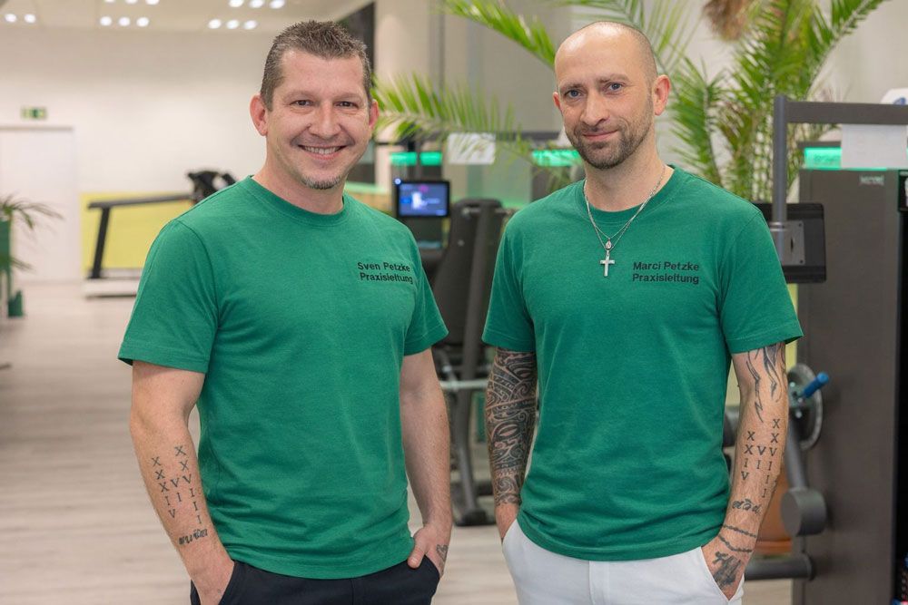 Zwei Männer in weißen Hemden umarmen sich lächelnd. Einer trägt eine Baseballkappe. Grüner Hintergrund.