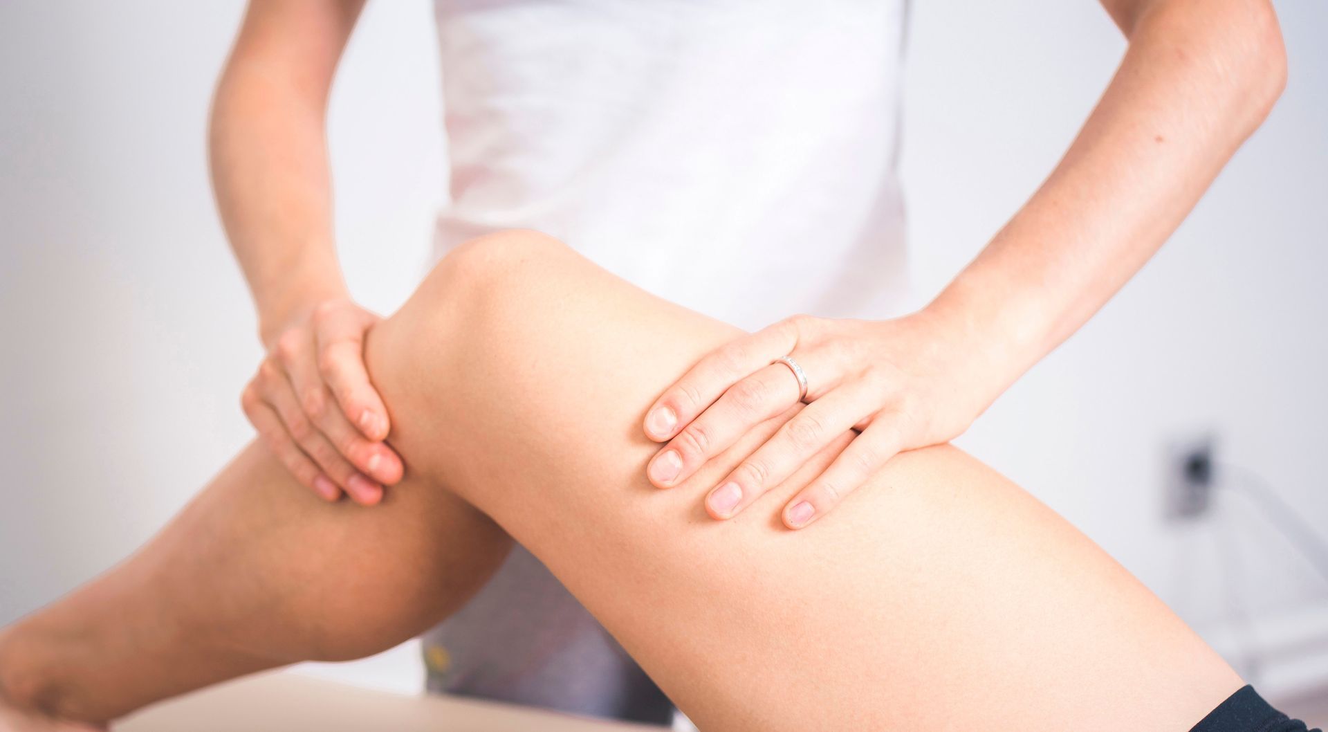 Therapeut behandelt das Knie eines Patienten. Weißes Hemd, Nahaufnahme, in einem hell erleuchteten Raum.