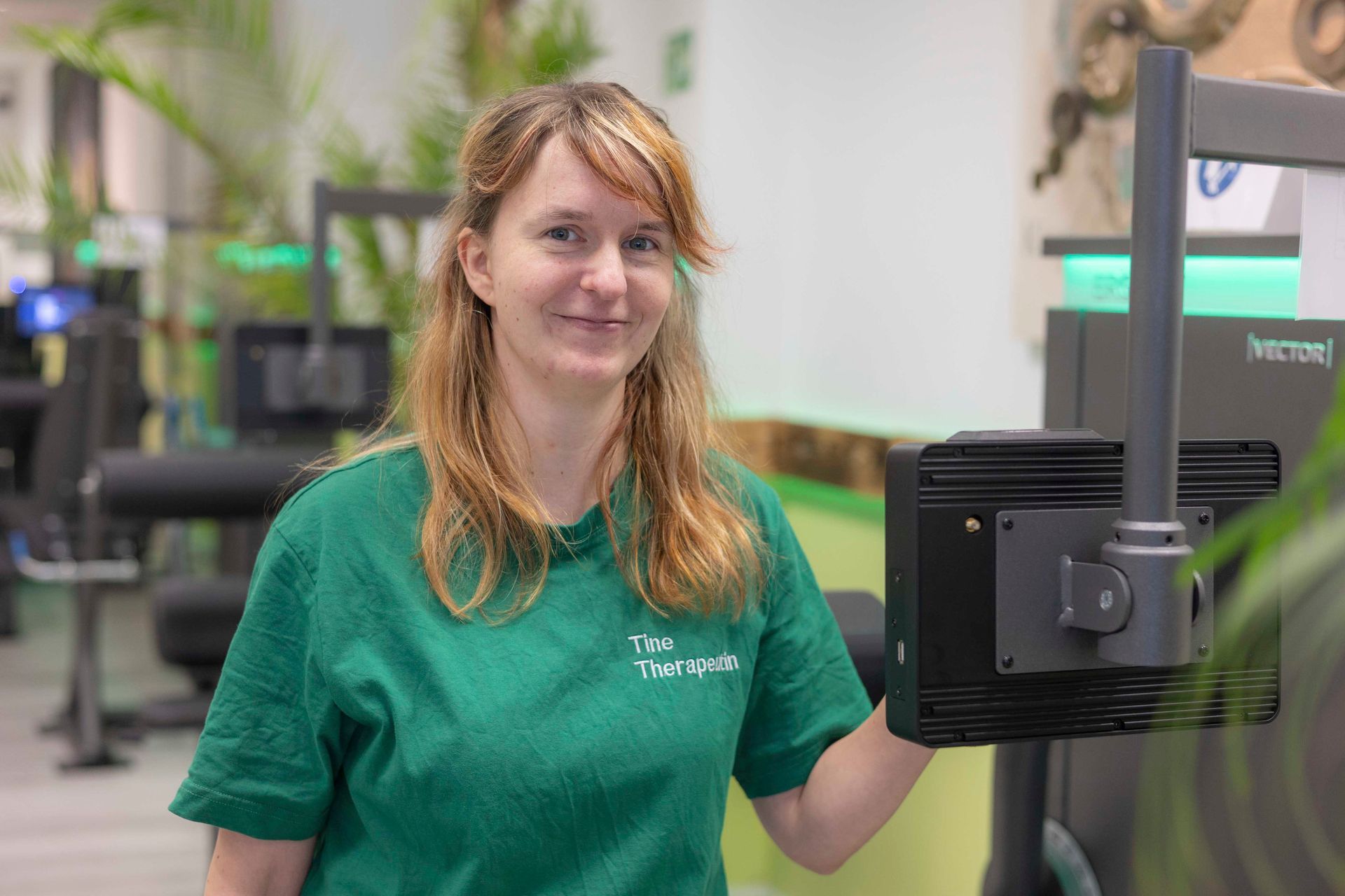 Frau in beigem Kapuzenpulli lächelt in die Kamera, grüner Hintergrund.