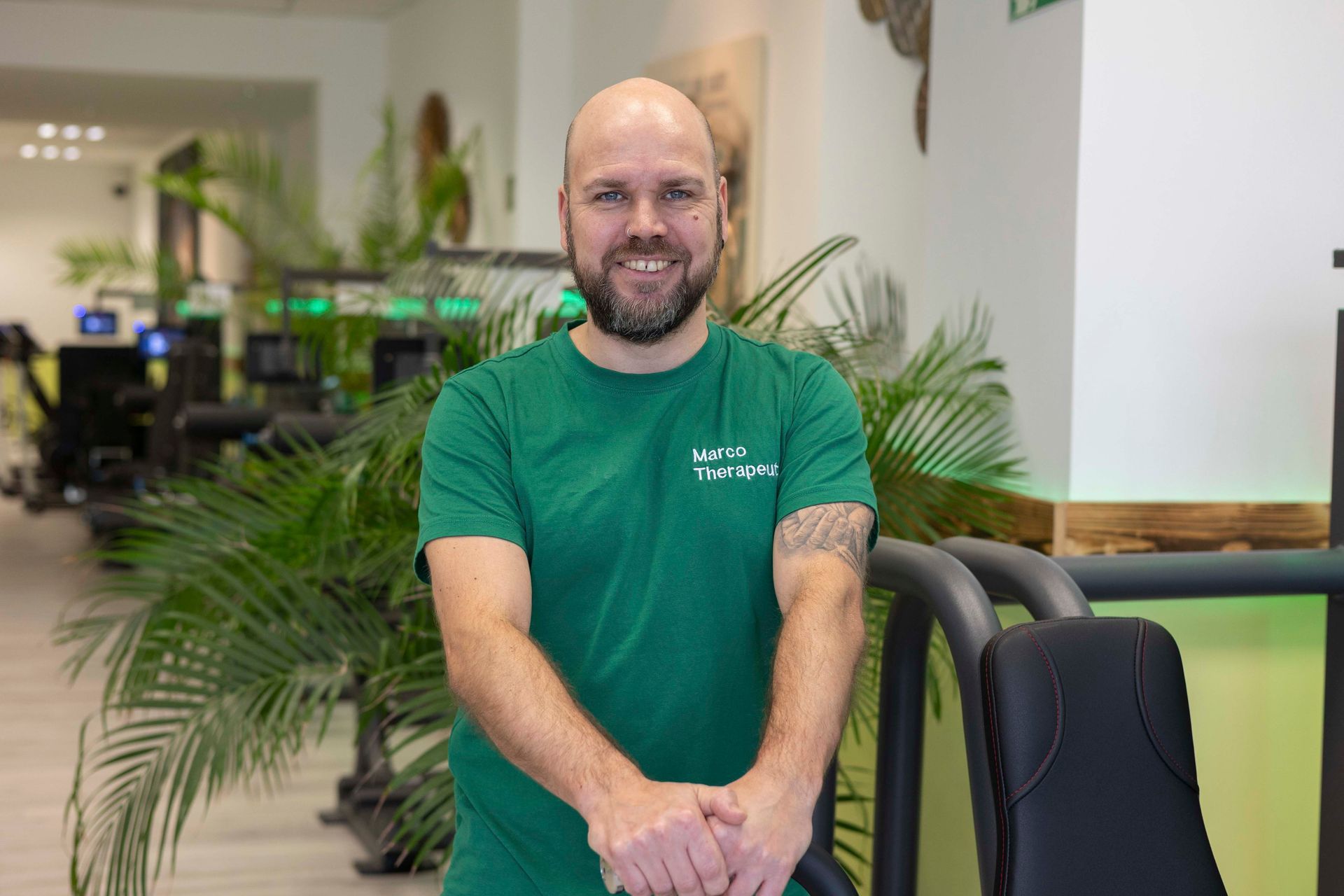 Ein bärtiger Mann mit Glatze lächelt. Er trägt ein graues Hemd und steht vor einem grünen Hintergrund.