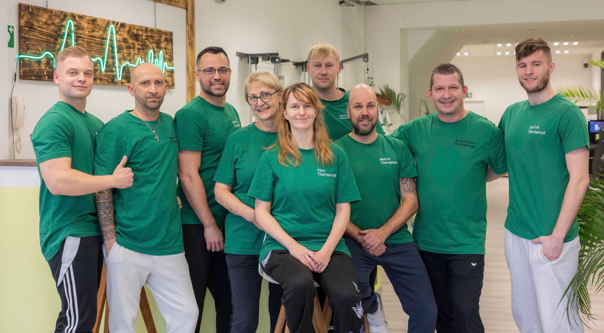 Eine Gruppe von Menschen feiert in einem Physiotherapieraum. Ein Patient gibt dem Personal ein Faustgruß.