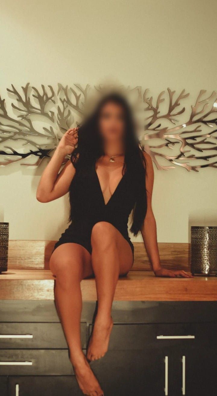 Una mujer con un vestido negro está sentada en una cómoda.