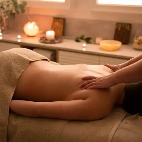 Persona recibiendo un masaje en una camilla en una cálida sala de spa iluminada con velas.