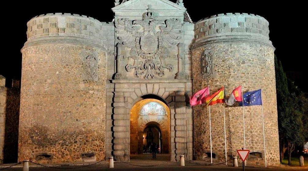 Un gran edificio de piedra con banderas ondeando frente a él por la noche.