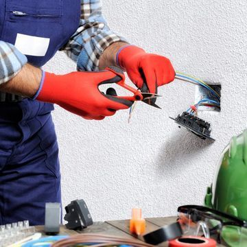 Un hombre que lleva guantes rojos está trabajando con cables eléctricos.