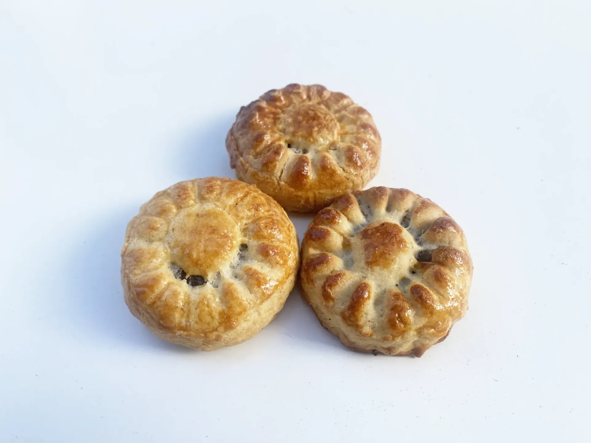 Tres pasteles redondos y dorados sobre fondo blanco. Cada uno tiene un borde ondulado decorativo y un relleno oscuro.