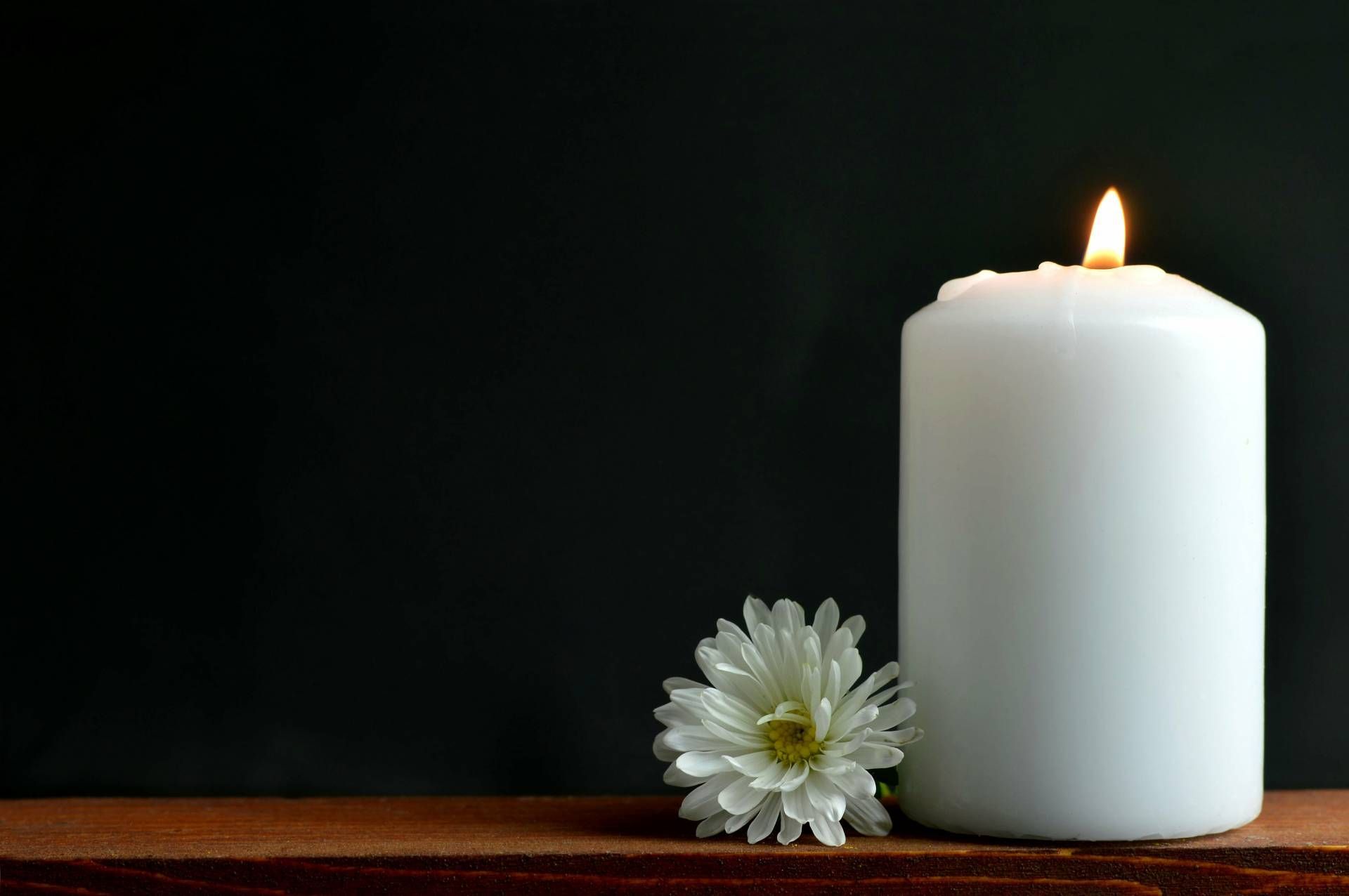 Eine weiße Kerze und eine weiße Blume stehen auf einem Holztisch.