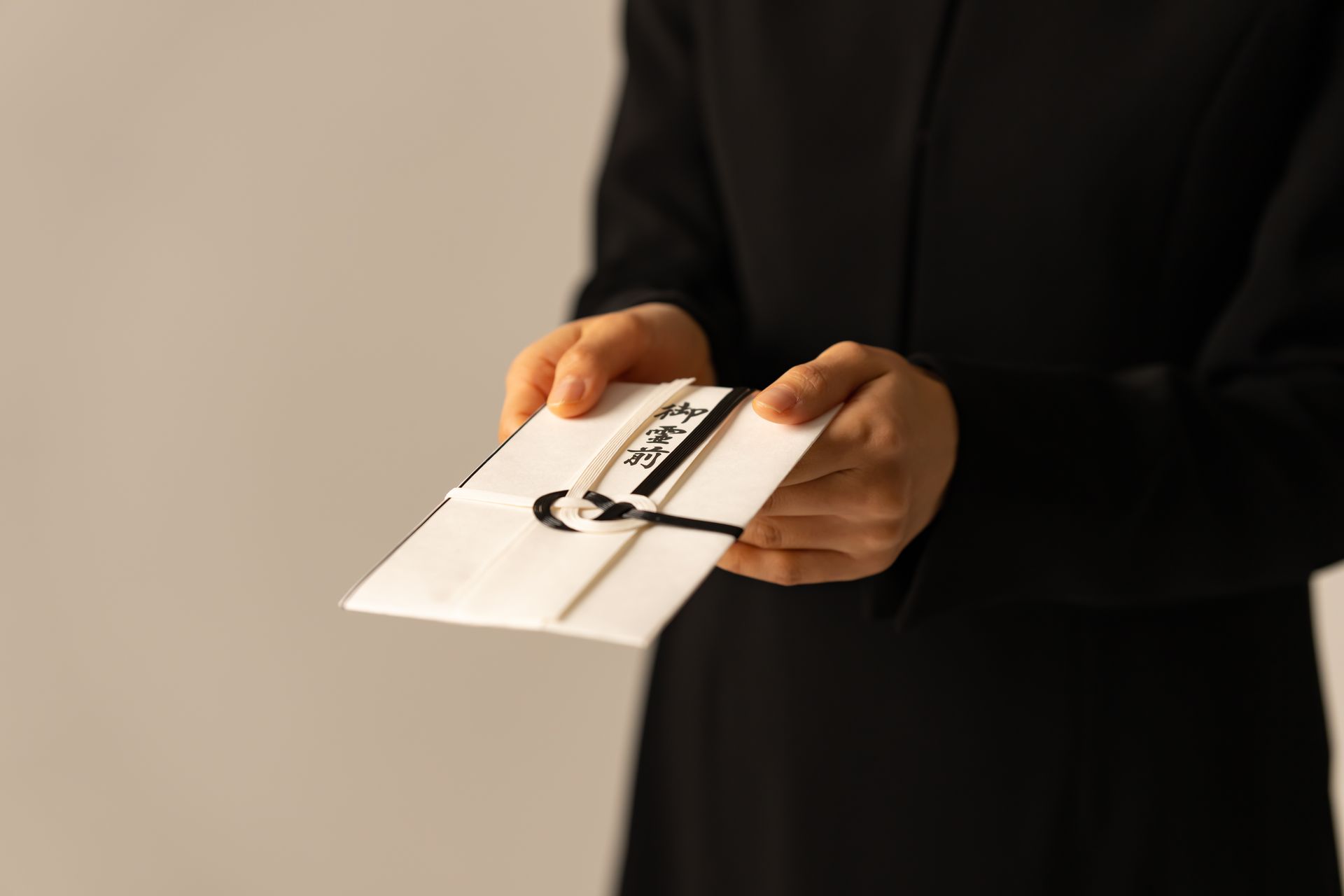 Eine Person in einem schwarzen Kleid hält einen weißen Umschlag in den Händen.
