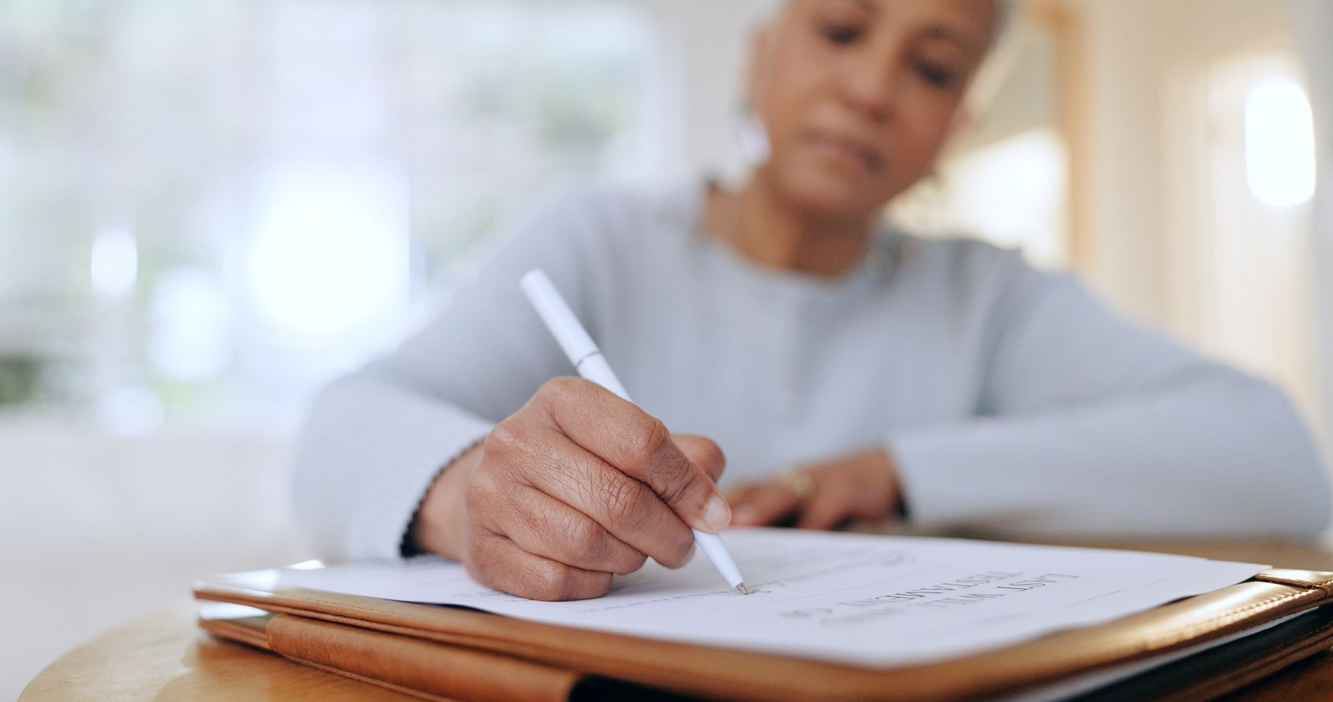 Eine Frau sitzt an einem Tisch und schreibt mit einem Stift auf ein Blatt Papier.