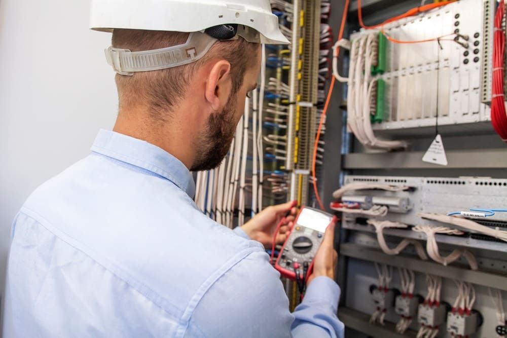 Un hombre con casco está trabajando en un panel eléctrico.