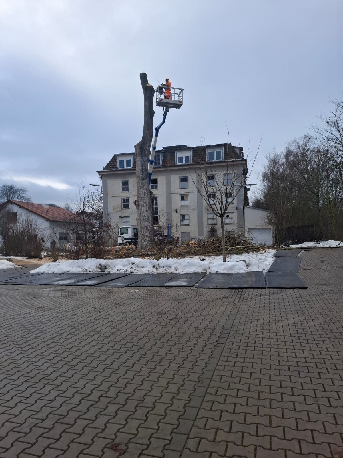 Baumpflege mit Hubsteiger neben Wohnhaus im Winter.