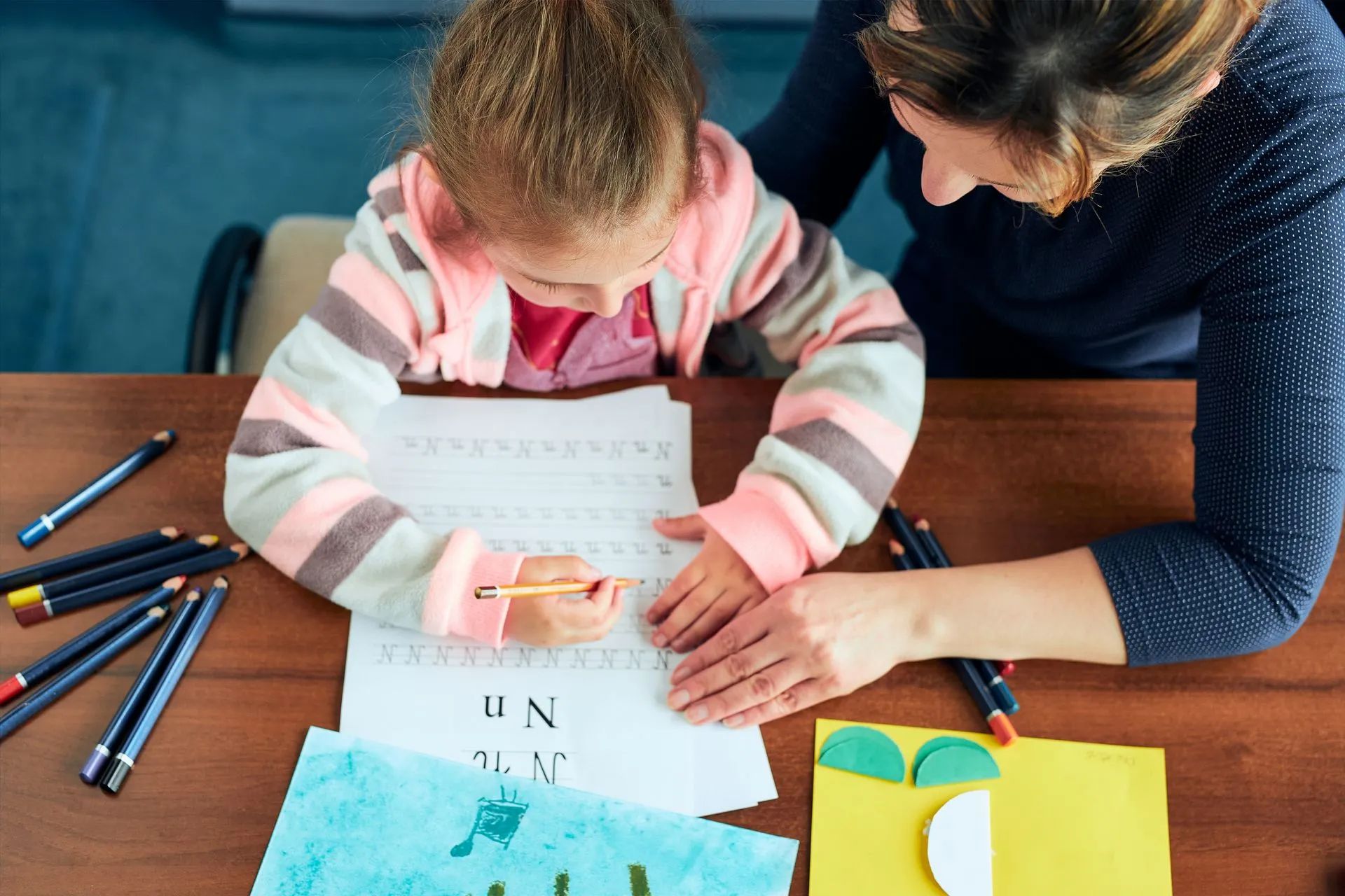 Un enfant colorie à une table avec des crayons et des feuilles de papier étalées