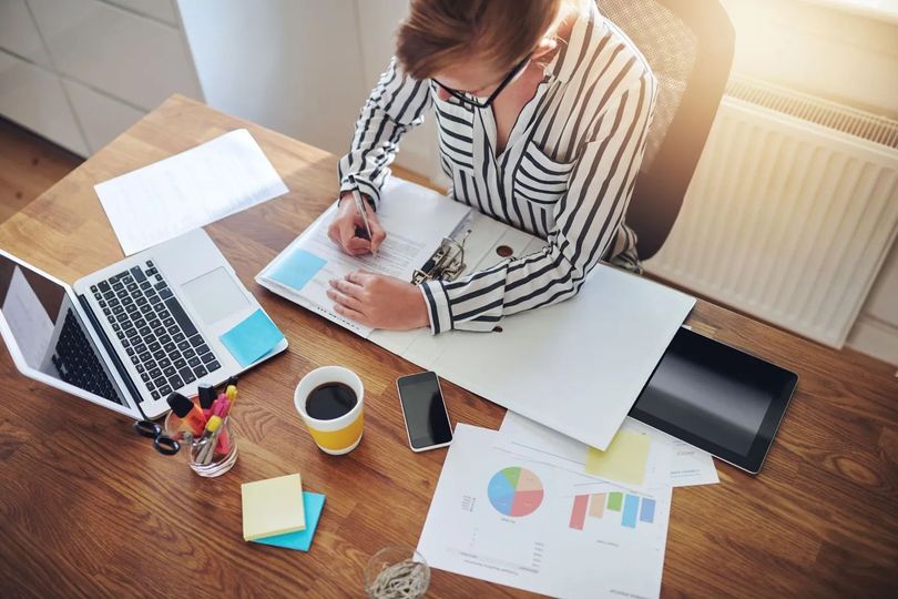 Une personne écrit à un bureau avec un ordinateur portable, du café et des graphiques