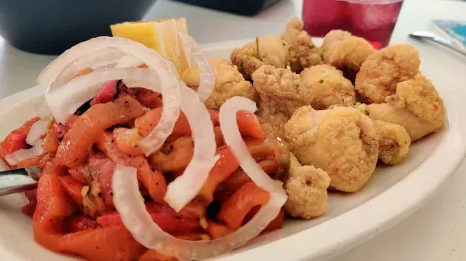Plato de comida frita con aros de cebolla, limón y un plato de comida roja.
