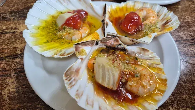 Vieiras de marisco servidas en sus conchas, cubiertas con salsa y guarnición, dispuestas en un plato.