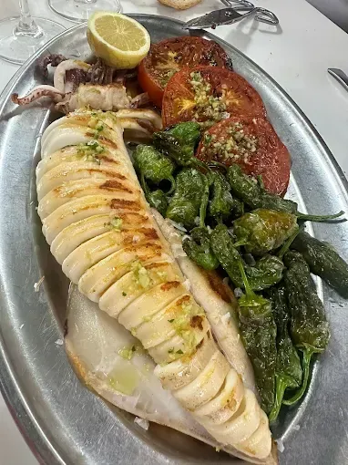 Plato de mariscos a la parrilla con calamares, tomates, pimientos verdes y limón.