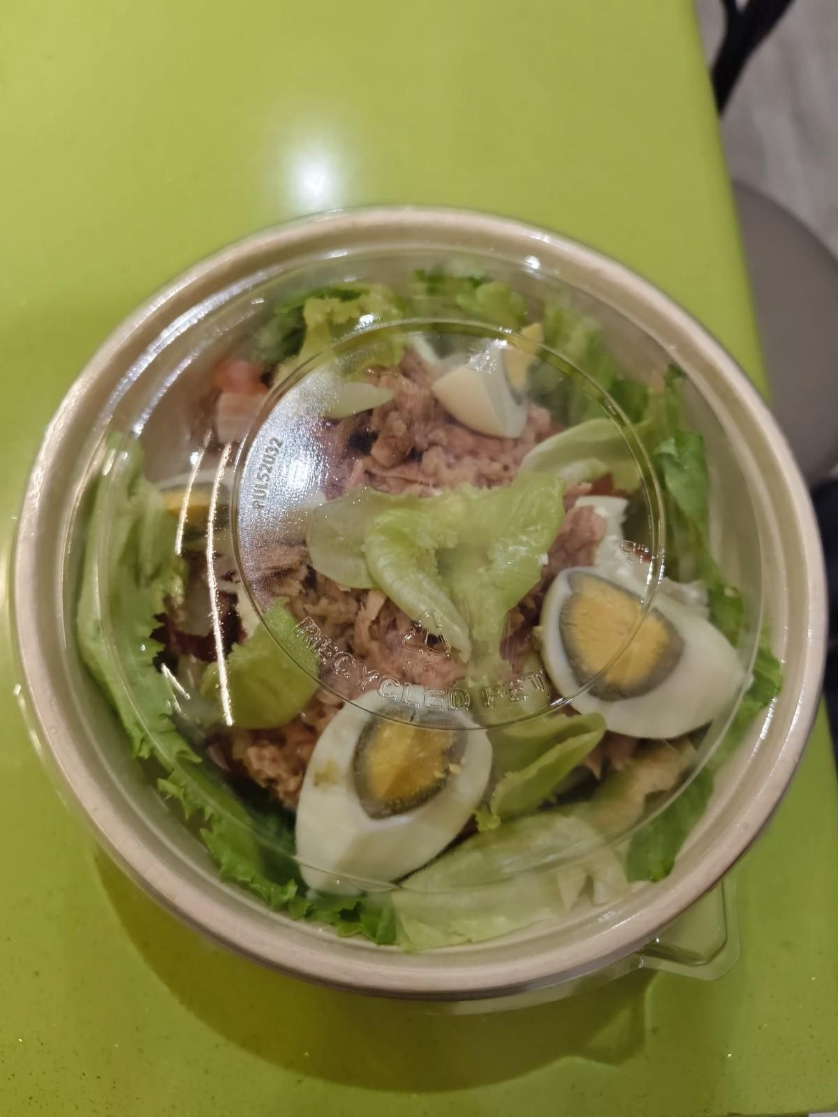 Vista desde arriba de una ensalada en un tazón transparente con lechuga, atún y huevos duros partidos por la mitad sobre una mesa verde.