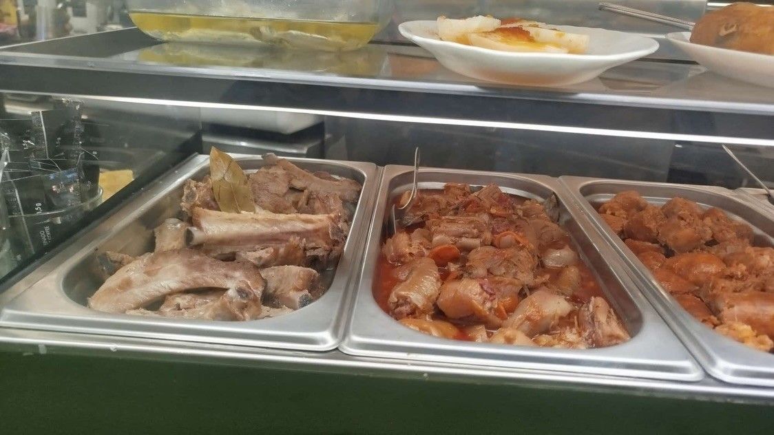 Tres bandejas de carne cocida y estofado en un mostrador de vidrio para exhibición de alimentos.