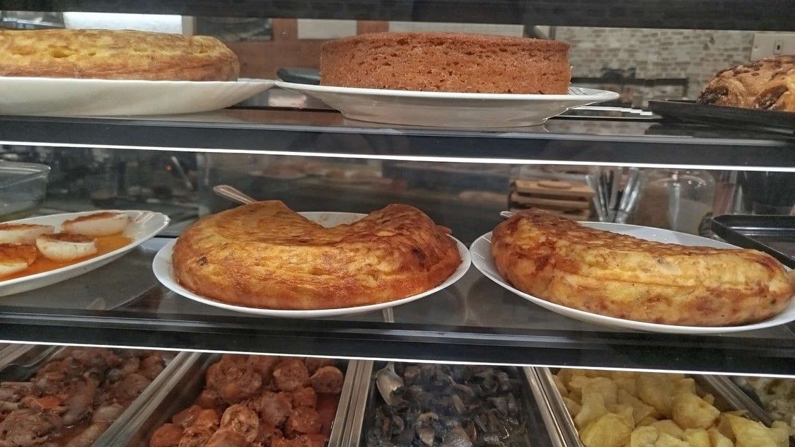 Vitrina de panadería con pasteles variados y productos horneados salados en bandejas de metal.