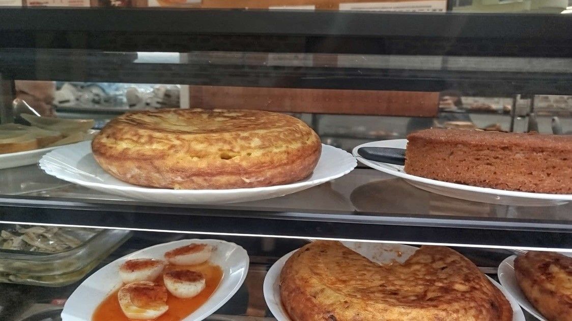 Pasteles y tartas expuestos en platos detrás de una vitrina de cristal de la pastelería.