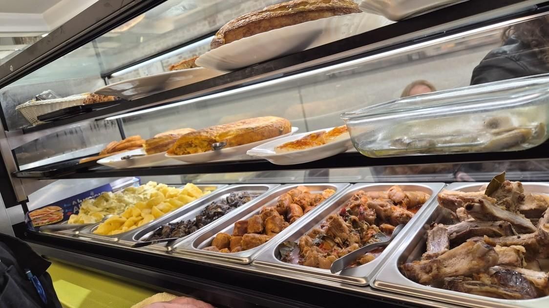 Vitrina de panadería con bandejas de pasteles y productos horneados variados bajo cristal.
