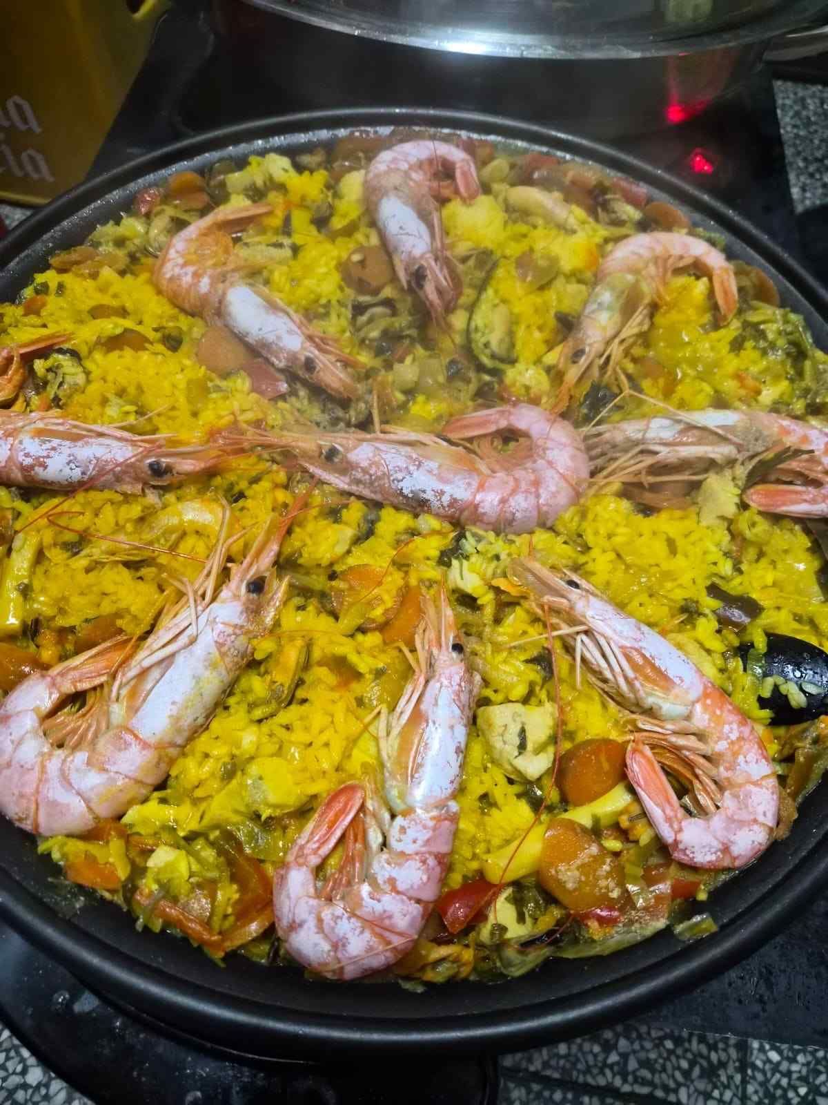 Paella de gambas en una sartén negra, cubierta con gambas rosadas y arroz amarillo.