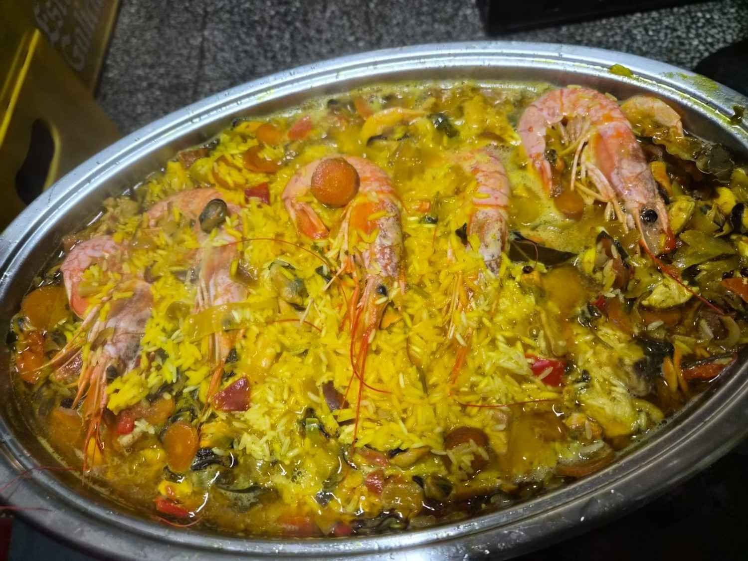 Bandeja ovalada de arroz amarillo con camarones, hierbas y verduras, servida caliente sobre una mesa.