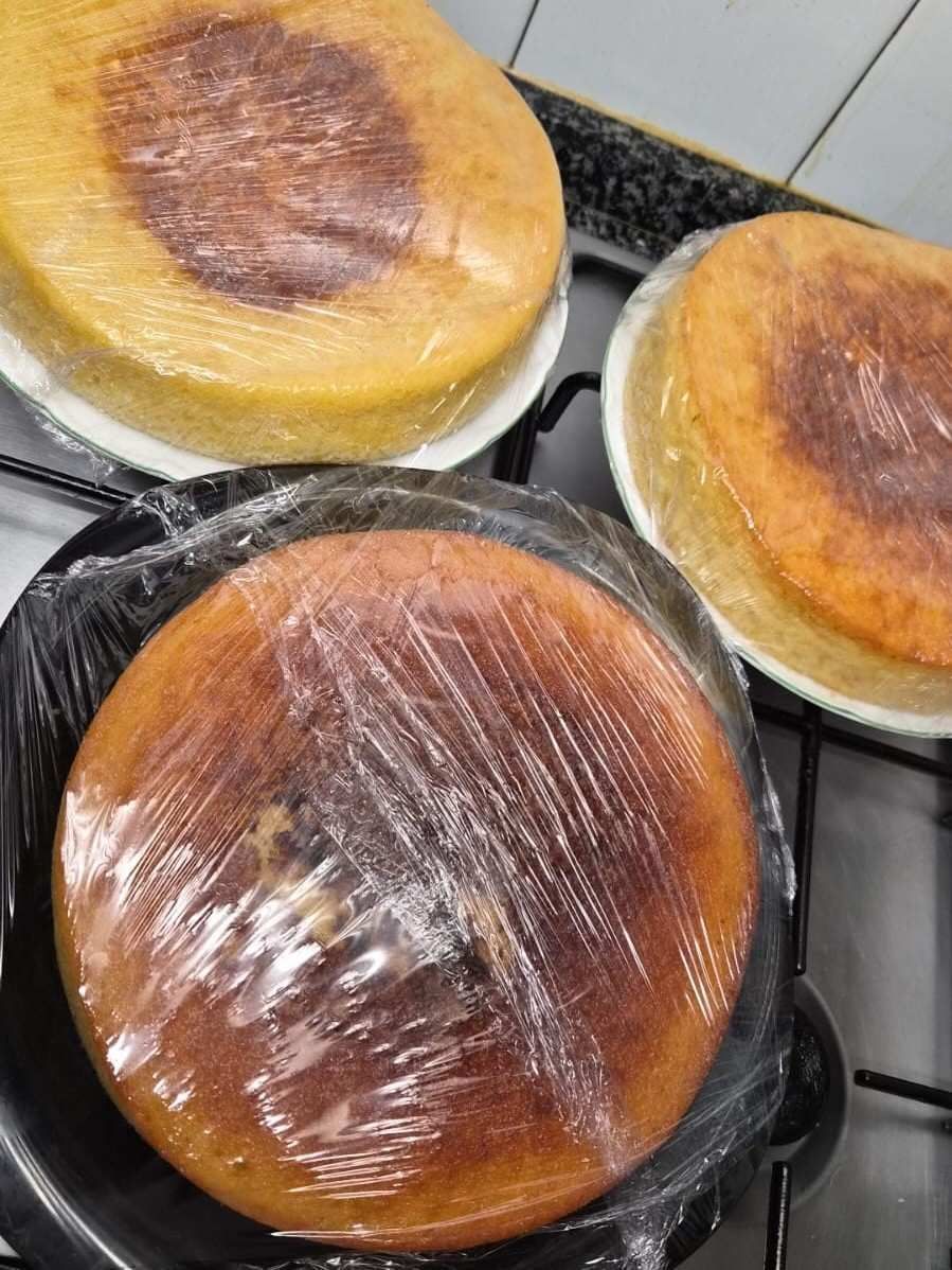 Tres pasteles redondos horneados en moldes sobre una estufa, cubiertos con film transparente.