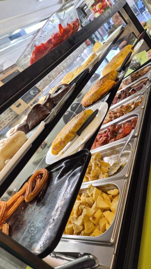 Variedad de pasteles y postres expuestos en una vitrina de cristal con bandejas metálicas.