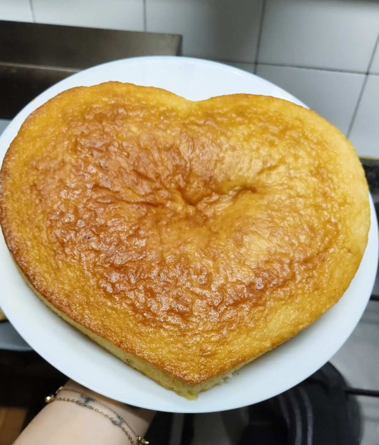 Pastel dorado horneado en forma de corazón sobre un plato blanco en una cocina.