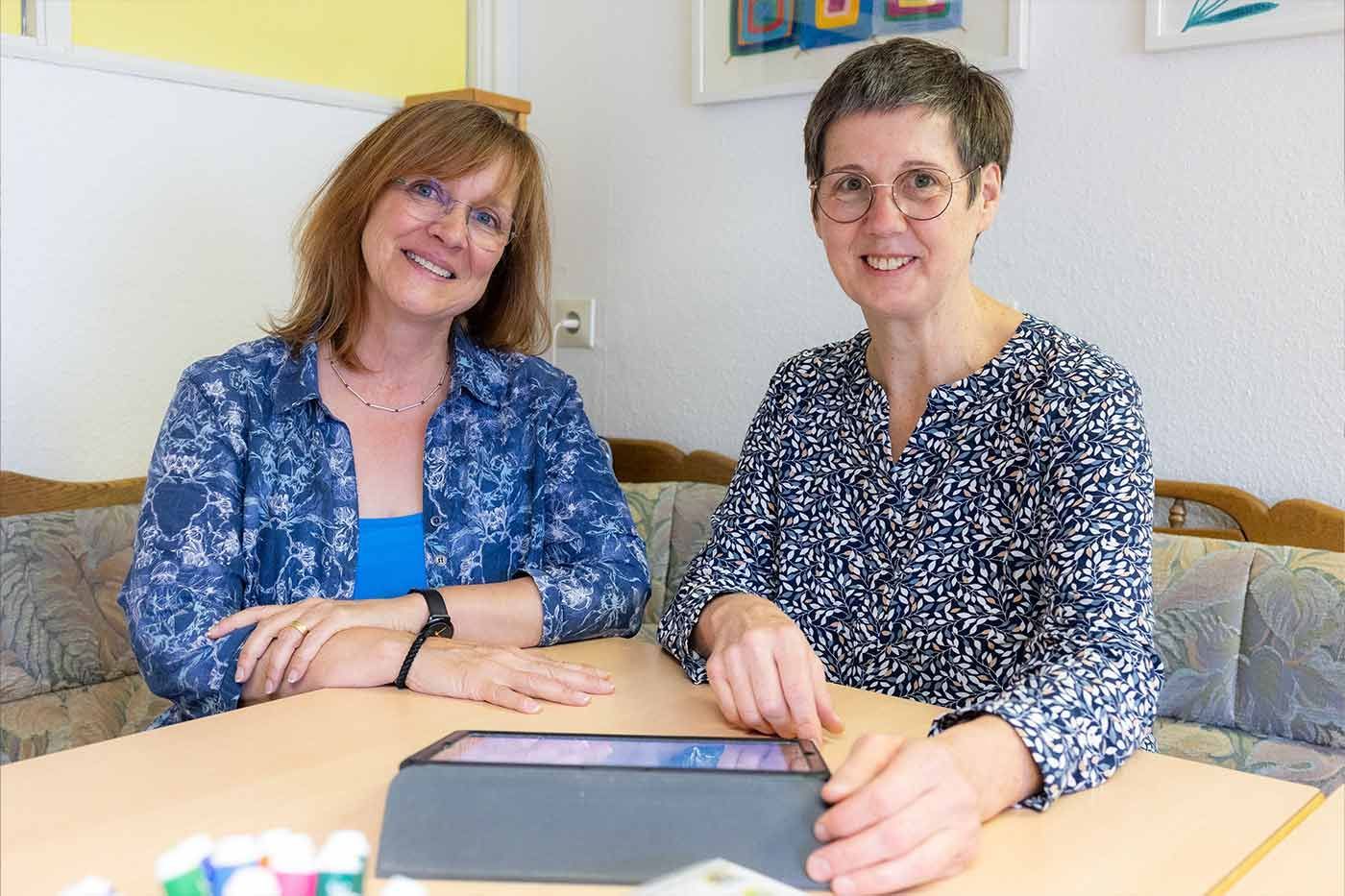 Zwei Frauen sitzen mit einem Tablet an einem Tisch.