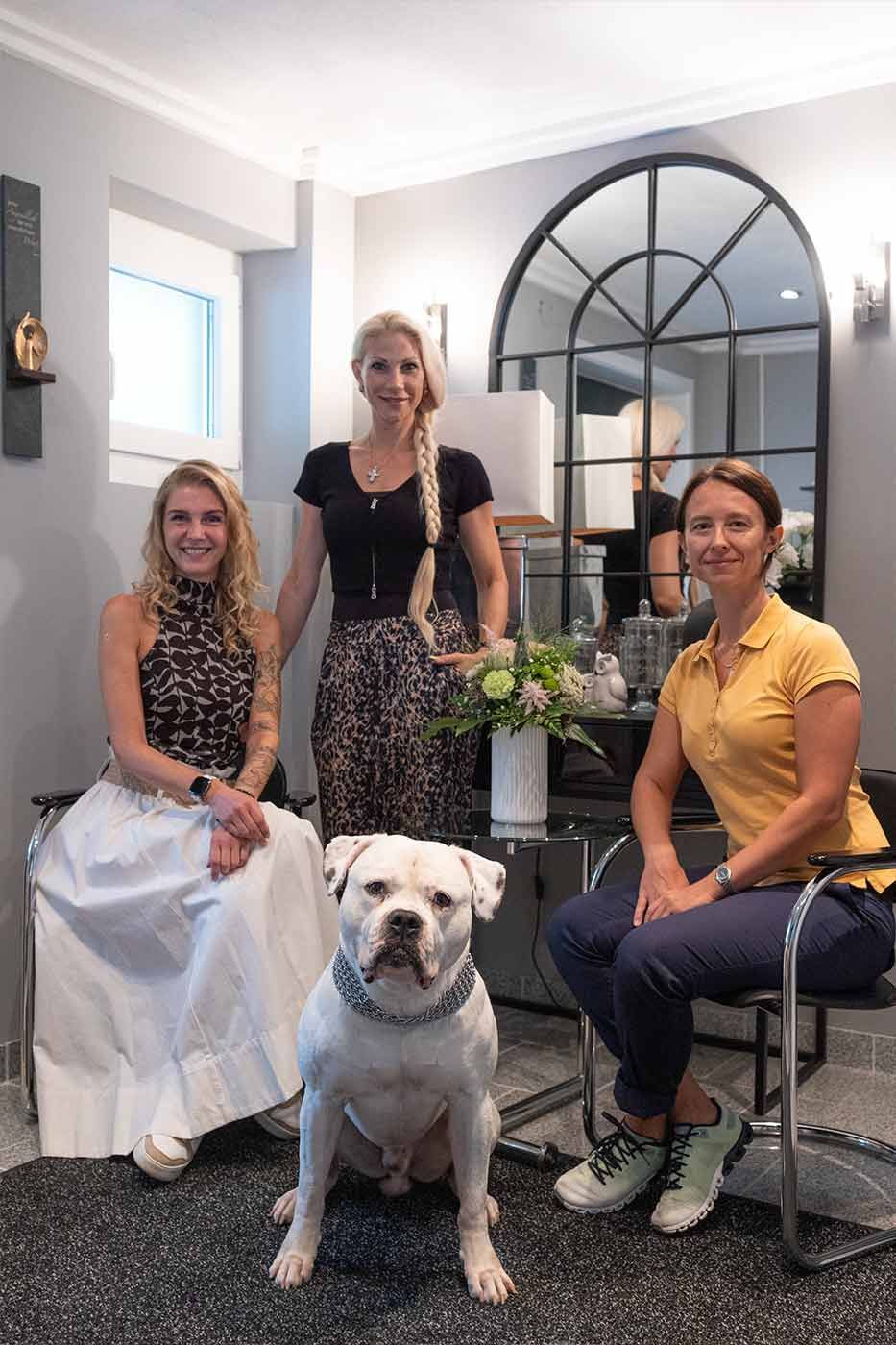 Drei Frauen und ein Hund posieren in einem Raum für ein Foto.