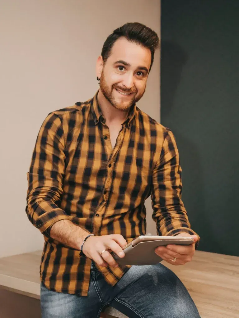 Un hombre con una camisa a cuadros está sentado en una mesa sosteniendo una tableta.