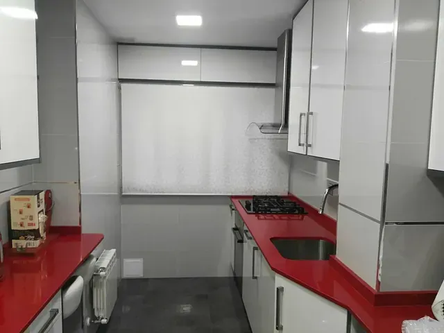 Una cocina con encimeras rojas y gabinetes blancos.