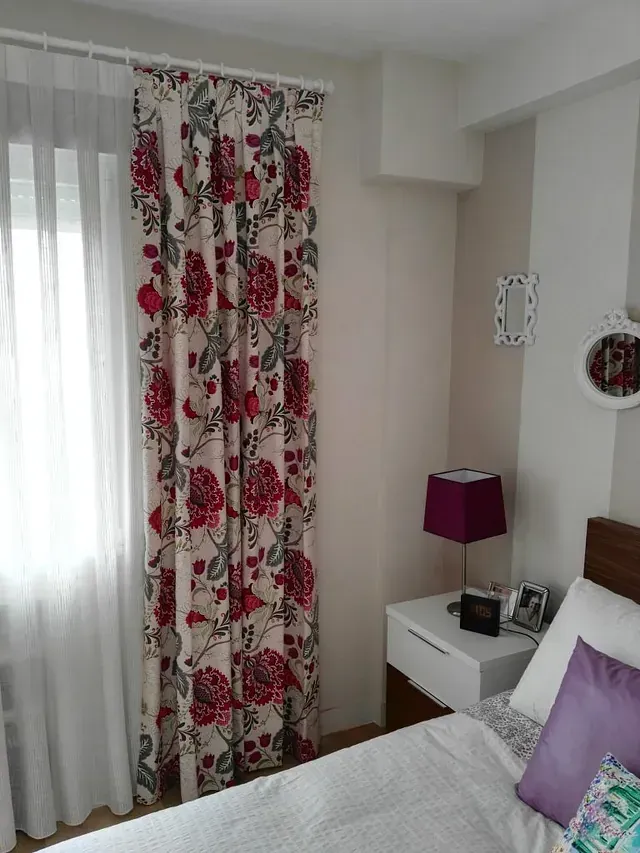 Un dormitorio con cama, mesita de noche, lámpara y cortinas florales.