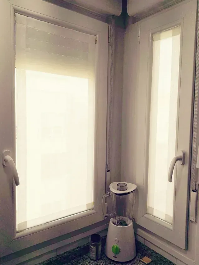 Una licuadora está en la esquina de una cocina al lado de una ventana.