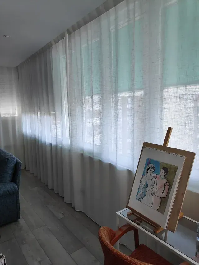 Una sala de estar con cortinas blancas y un cuadro en un caballete.