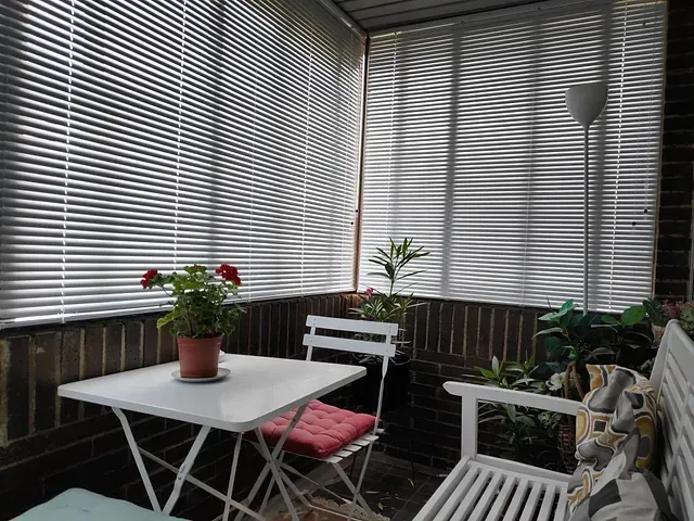 Hay una mesa y sillas en el balcón con persianas.