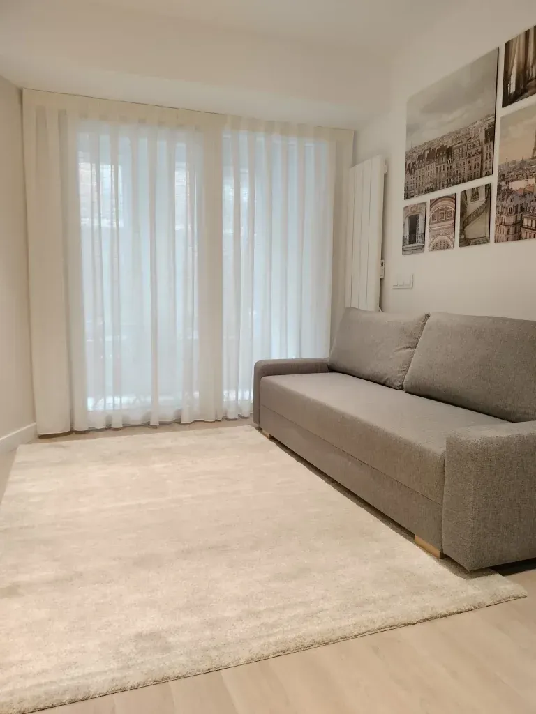 Una sala de estar con sofá, alfombra y grandes ventanales.