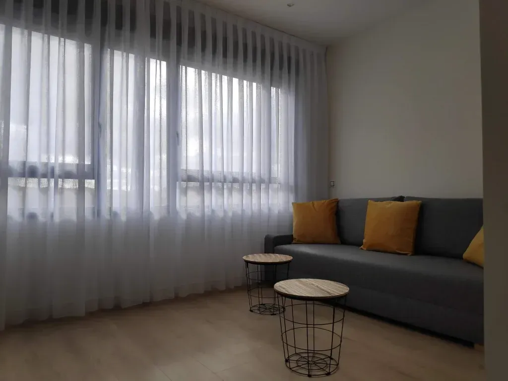 Una sala de estar con un sofá y dos mesas frente a una ventana.