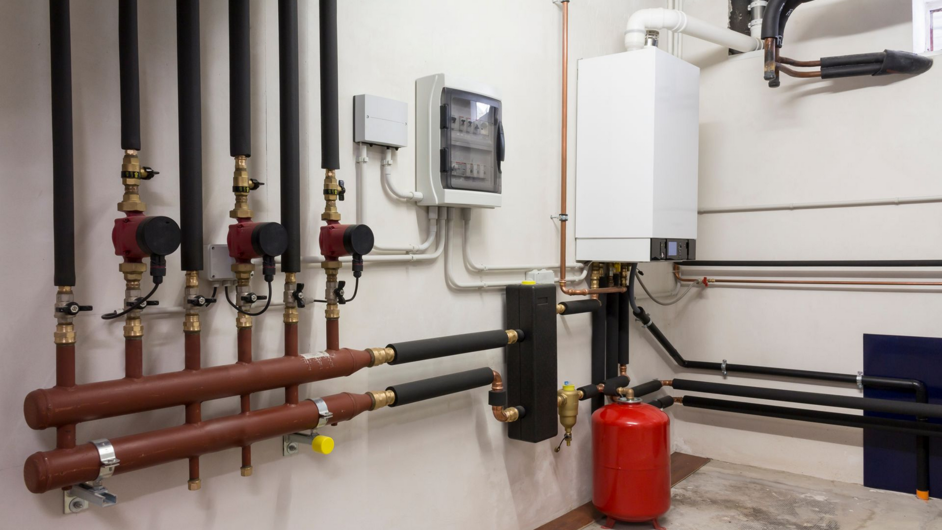 Composants du système de chauffage : tuyaux, pompes, chaudière, vase d'expansion rouge.