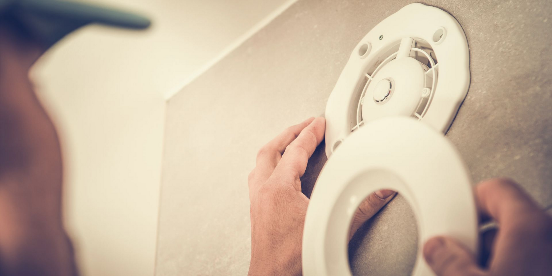 Personne installant un une bouche d'aération sur un mur de salle de bain.