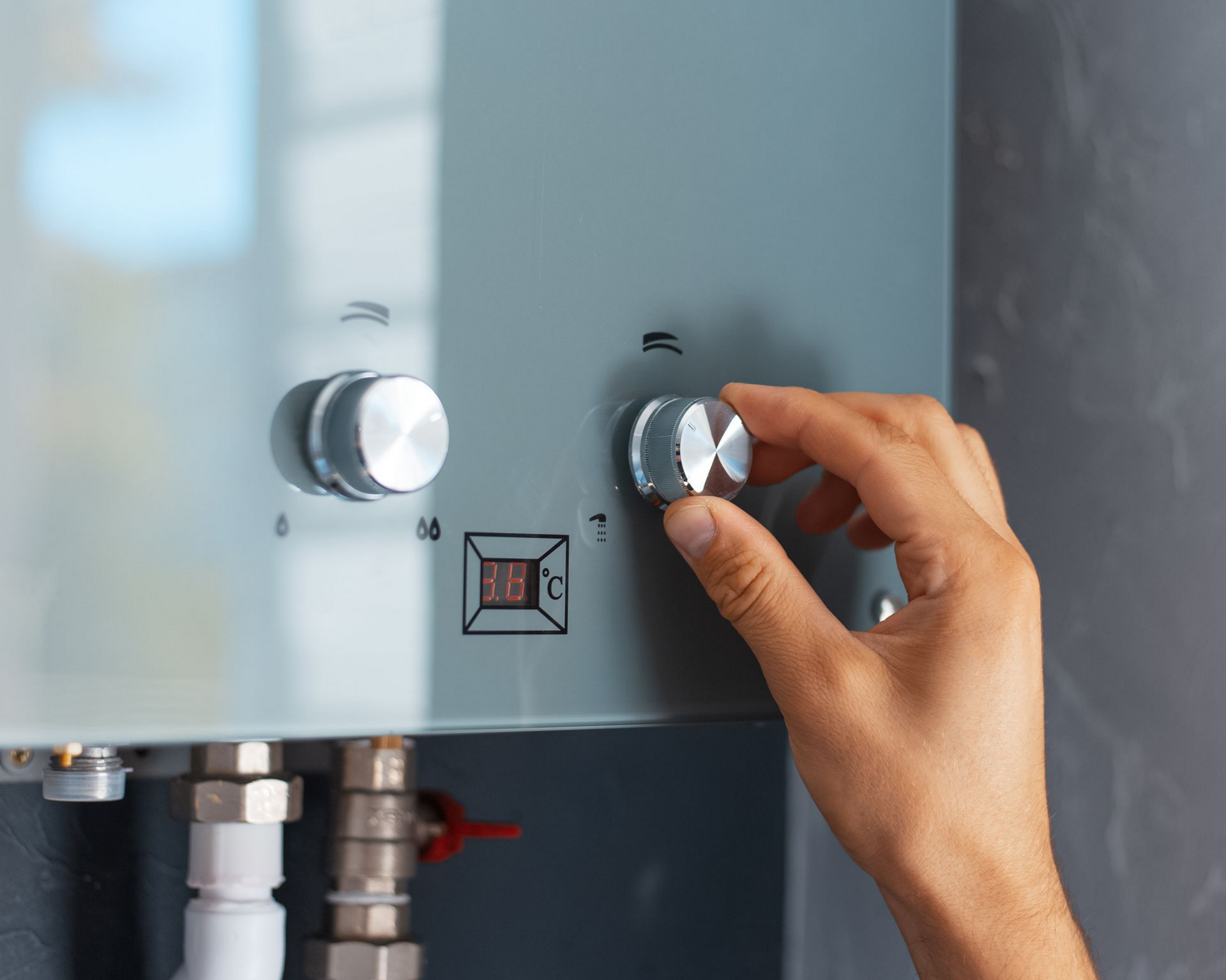 Main tournant le bouton d'un chauffe-eau gris. L'affichage numérique indique la température.