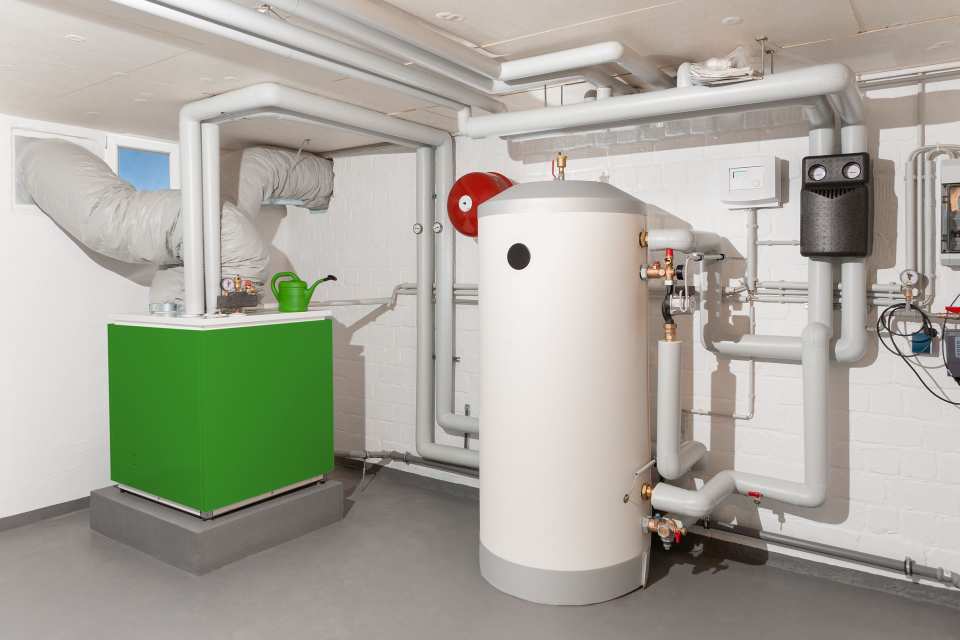 Fournaise et chauffe-eau verts dans une buanderie au sous-sol avec tuyaux et évent.