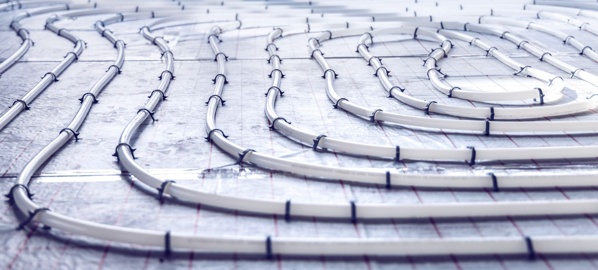 Tuyaux de chauffage par le sol radiant blancs posés sur une surface en béton.