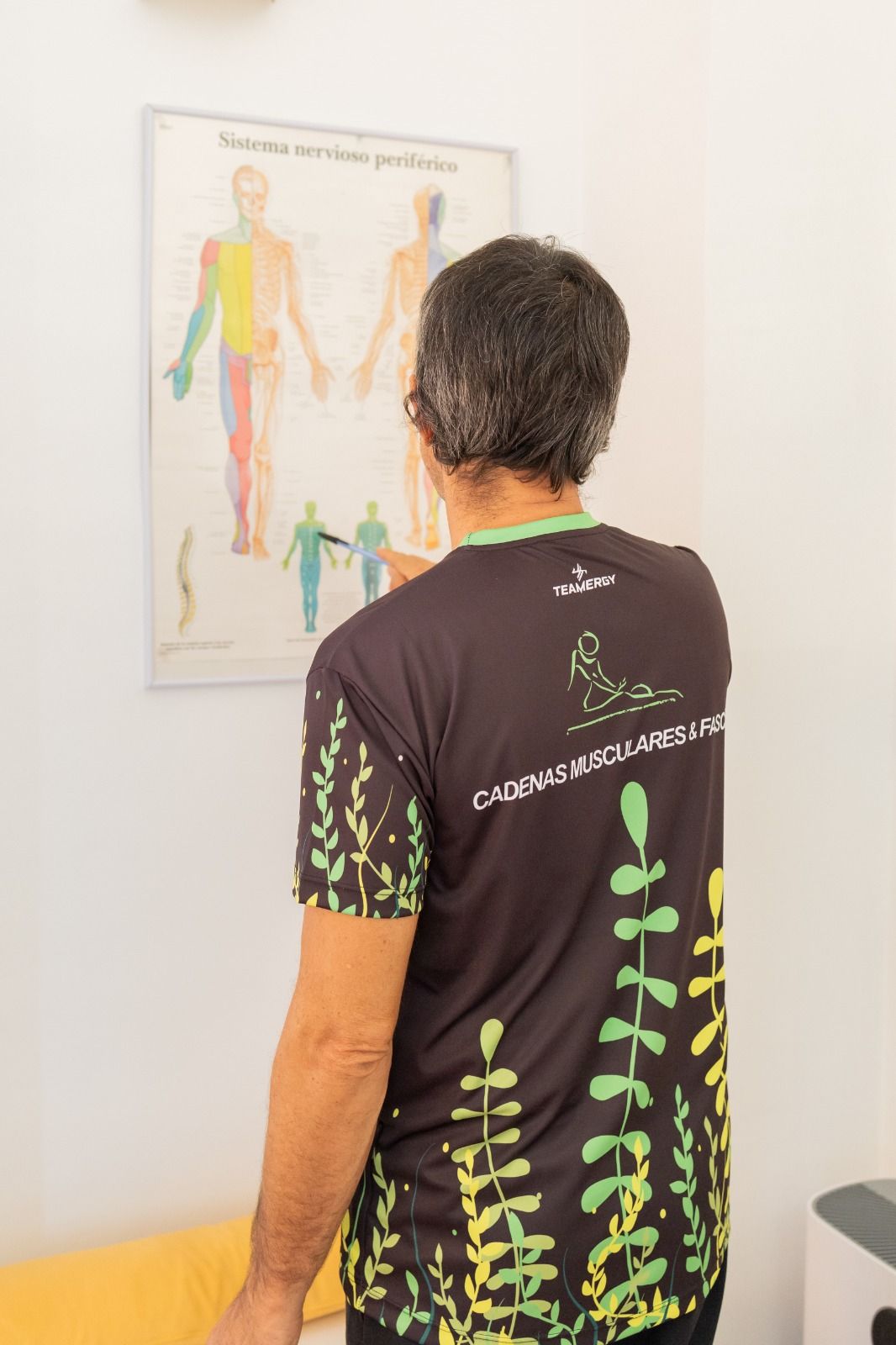 Un hombre con una camisa negra está parado frente a un diagrama del cuerpo humano.