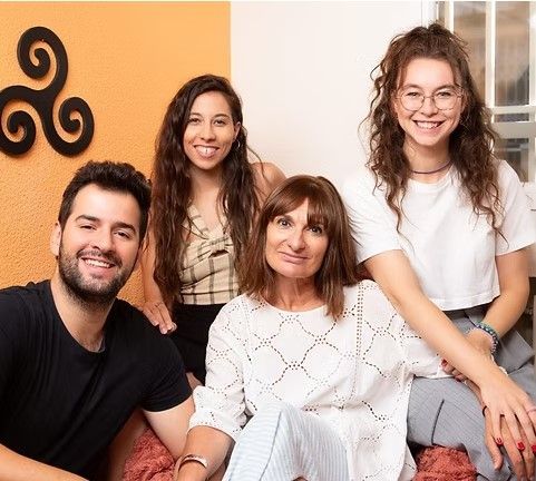 Cuatro personas sonrientes posan juntas: un hombre, dos mujeres y una mujer más joven, en el interior.